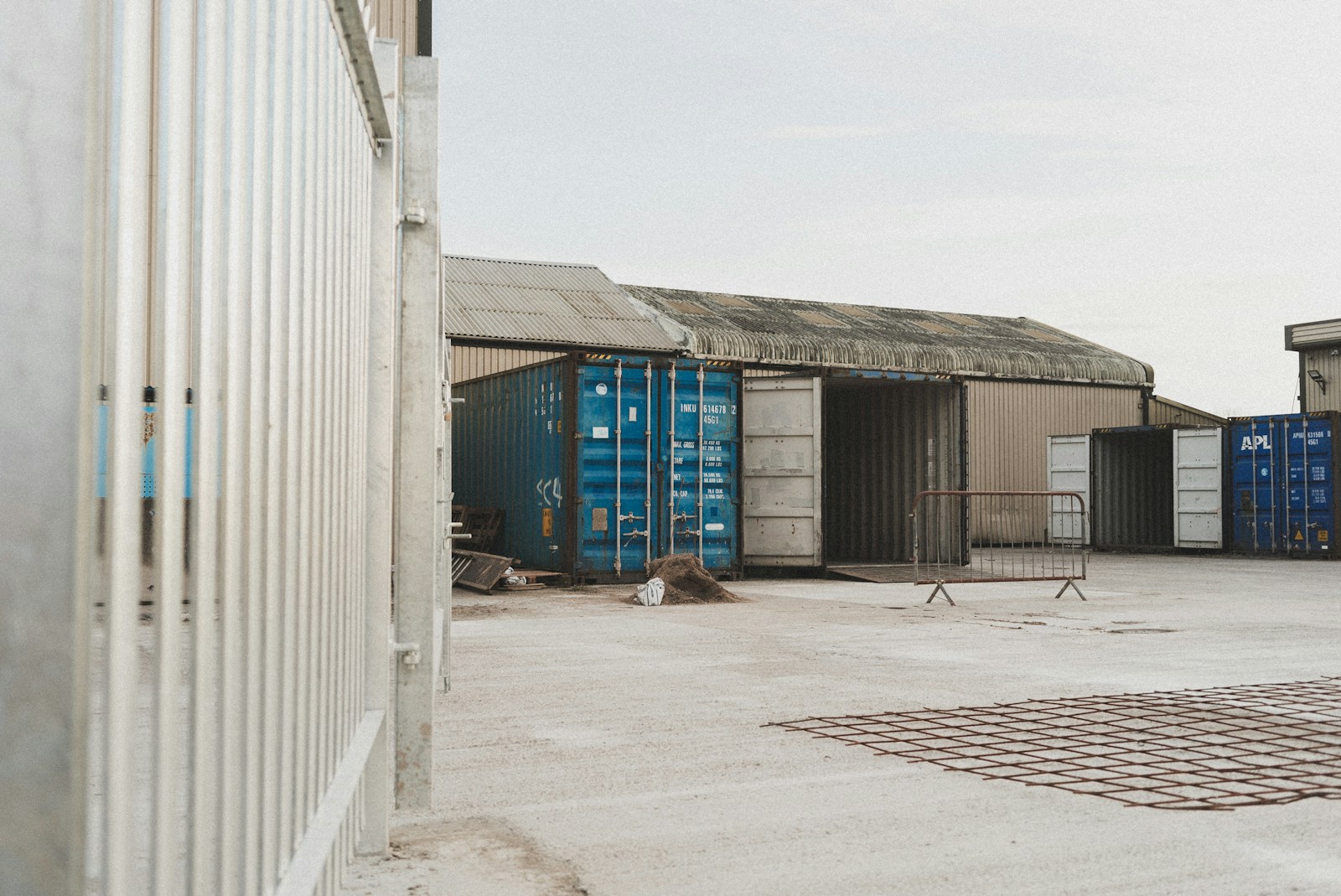 Blue and white shipping containers with open doors in an industrial yard.