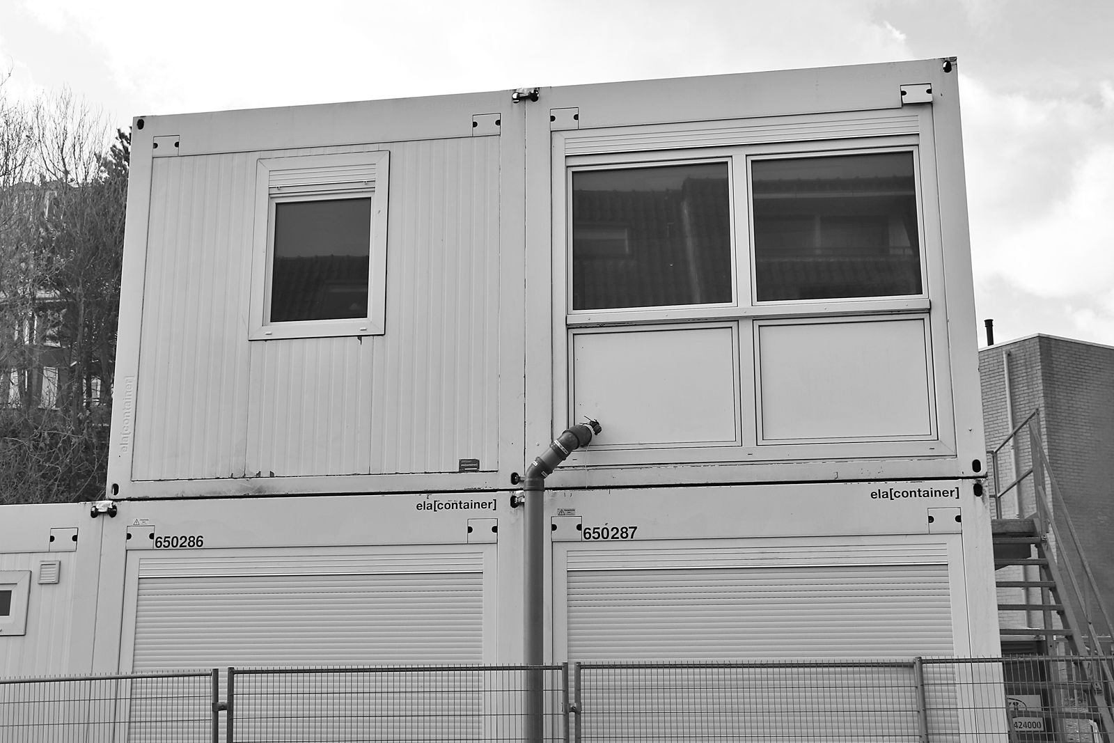 Black-and-white photograph of stacked modular office units with windows at a construction site.