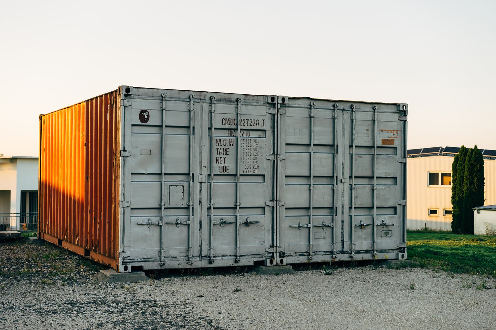 Two weathered steel shipping containers on a gravel surface in warm sunlight.